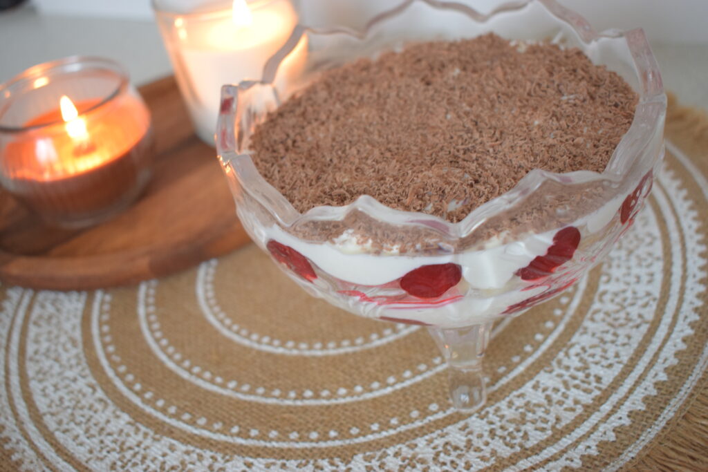 Close-up of a no-bake cherry tiramisu cake in a glass bowl with layered cream, ladyfingers, and grated chocolate on top